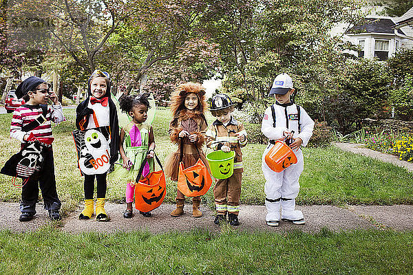 Kinder in voller Länge in Halloween-Kostümen  die während eines Streiches oder einer Behandlung auf dem Weg stehen