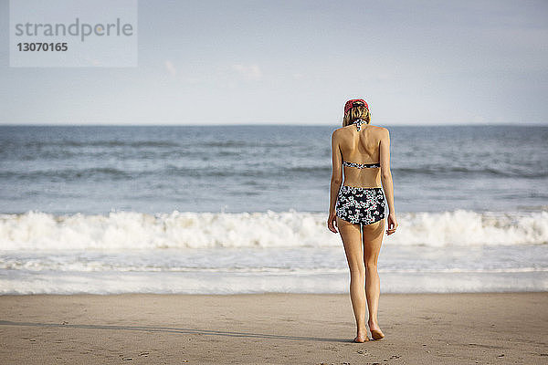 Rückansicht einer Frau  die am Strand am Ufer spazieren geht