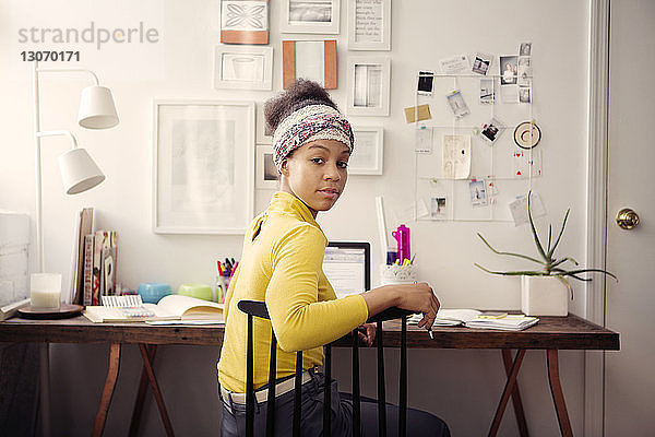 Porträt einer Frau  die am Laptop-Computer am Tisch gegen Papiere an der Wand arbeitet