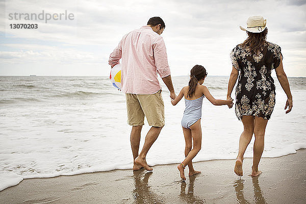 Rückansicht einer Familie  die am Strand vor bewölktem Himmel spazieren geht