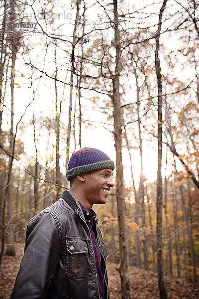 Lächelnder Mann steht im Winter an Bäumen im Wald