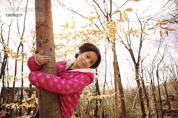 Porträt eines niedlichen Mädchens  das im Herbst im Hof einen Baumstamm umarmt