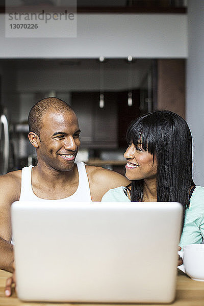 Lächelndes Paar mit Laptop-Computer  während es zu Hause am Tisch sitzt