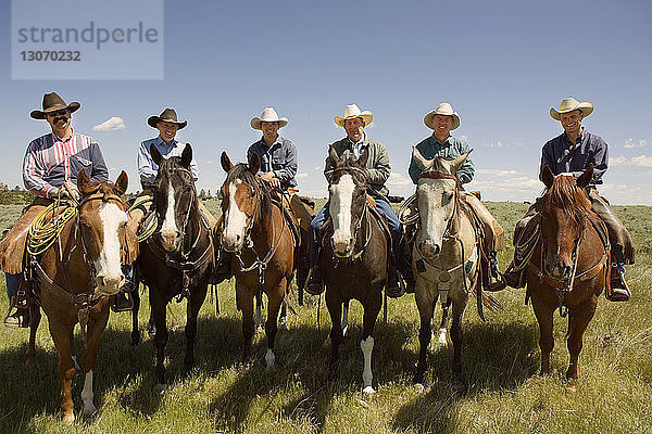 Porträt von Cowboys  die auf Pferden gegen den Himmel sitzen