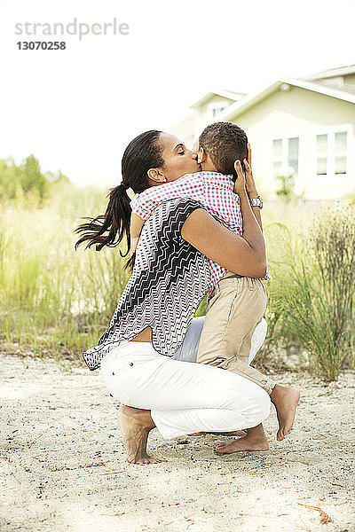 Glückliche Frau küsst Sohn im Hinterhof vor klarem Himmel