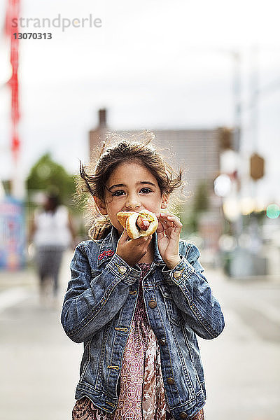 Mädchen isst Hot Dog im Stehen auf der Straße in der Stadt