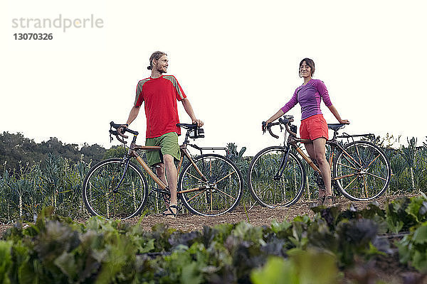 Niedrigwinkelansicht eines Paares mit Fahrrädern  das auf einem Bauernhof vor klarem Himmel steht