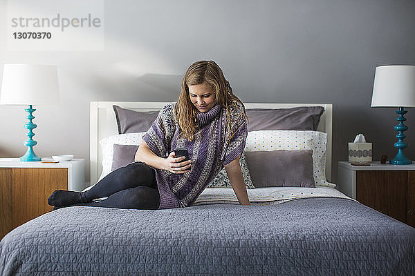 Frau benutzt Smartphone  während sie zu Hause im Bett sitzt