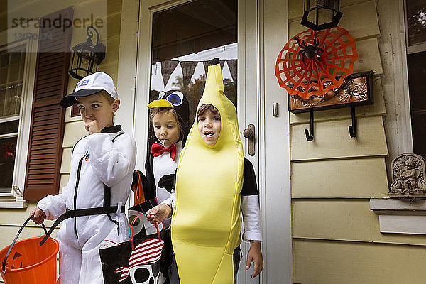 Kinder in Halloween-Kostümen  die bei Trick oder Behandlung gegen das Haus stehen