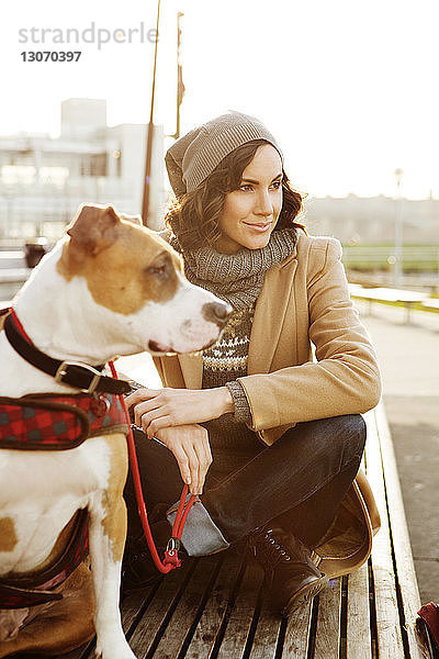 Frau mit Hund schaut weg  während sie auf einer Bank sitzt