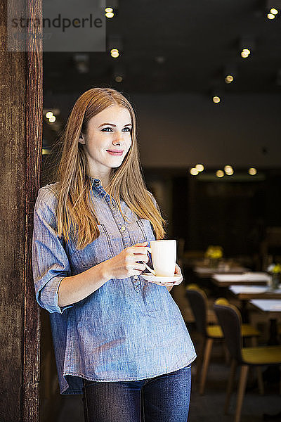 Nachdenklich lächelnde Frau  die eine Kaffeetasse hält  während sie im Café steht