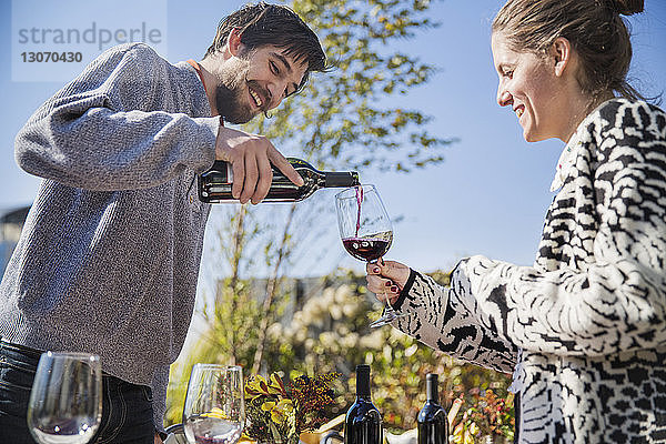 Niedrigwinkelansicht eines Mannes  der während einer Gartenparty Rotwein für eine Freundin einschenkt