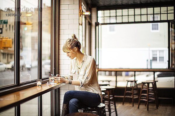 Frau benutzt Smartphone  während sie auf einem Hocker in einer Bar sitzt