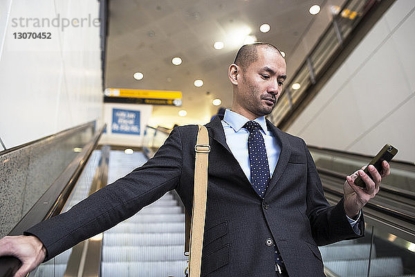 Geschäftsmann benutzt Mobiltelefon  während er auf der Rolltreppe in der U-Bahn-Station steht