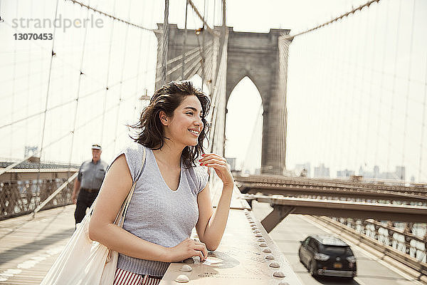 Lächelnde Frau steht an der Brooklyn Bridge in der Stadt