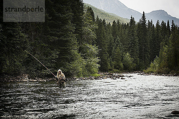 Älterer Mann fischt im Fluss gegen Wald