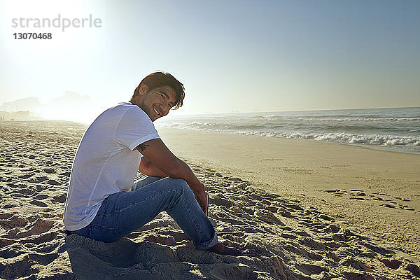Porträt eines lächelnden Mannes  der auf Sand am Strand sitzt