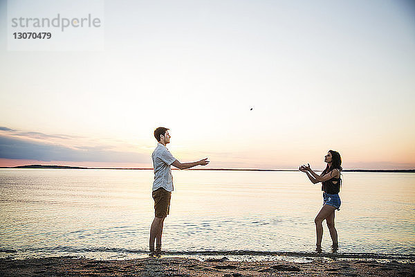 Freunde spielen mit Stein am Strand gegen den Himmel bei Sonnenuntergang