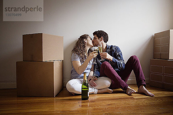 Paar mit Weingläsern  die sich küssen  während sie zu Hause auf dem Boden sitzen
