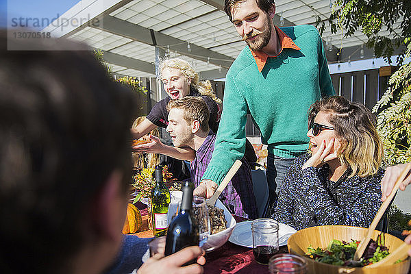 Mann serviert Freunden während einer Gartenparty Essen
