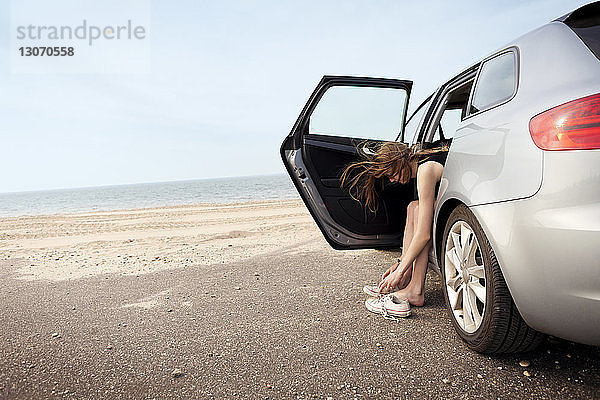 Frau trägt Schuhe  während sie am Strand im Auto sitzt