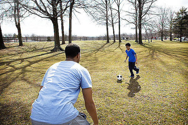 Vater spielt Fussball mit Sohn auf dem Spielfeld im Park