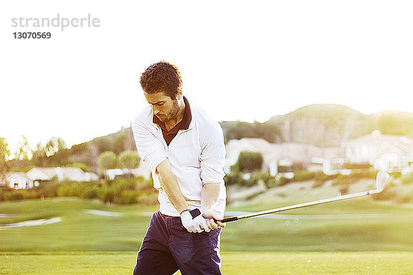 Mann hält Golfschläger  während er gegen den klaren Himmel steht