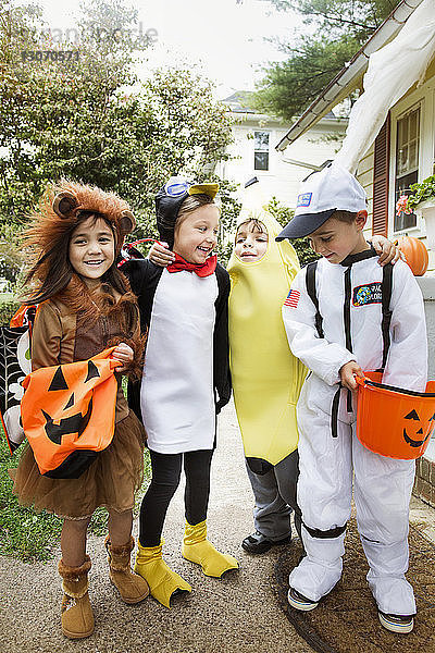 Fröhliche Kinder in Halloween-Kostümen in voller Länge  die während eines Streichs oder einer Behandlung im Hof stehen