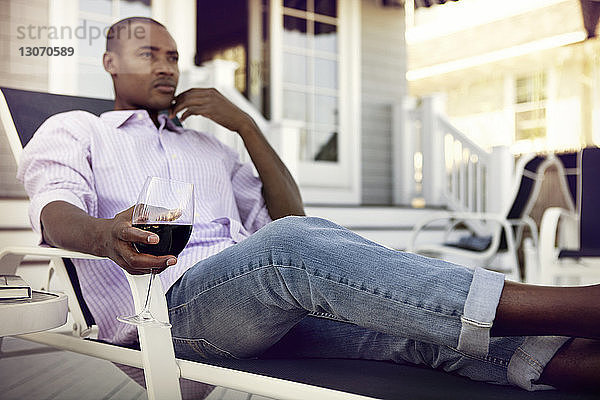 Nachdenklicher Mann hält Weinglas  während er auf einem Liegestuhl sitzt