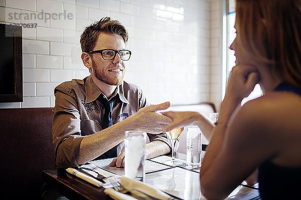 Mann hält die Hand seiner Freundin  während er im Restaurant sitzt