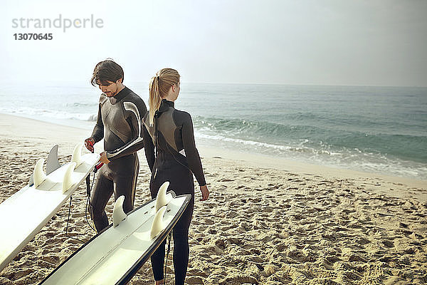 Mann und Frau in Neoprenanzügen stehen am Strand an den Surfbrettern