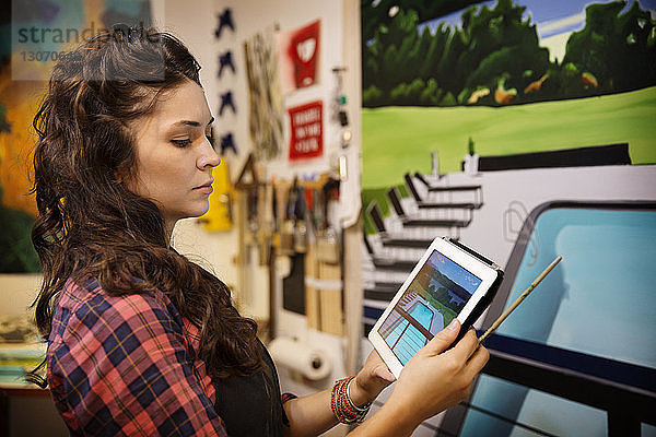 Seriöse Frau betrachtet Tablet-Computer gegen Malerei an der Wand zu Hause