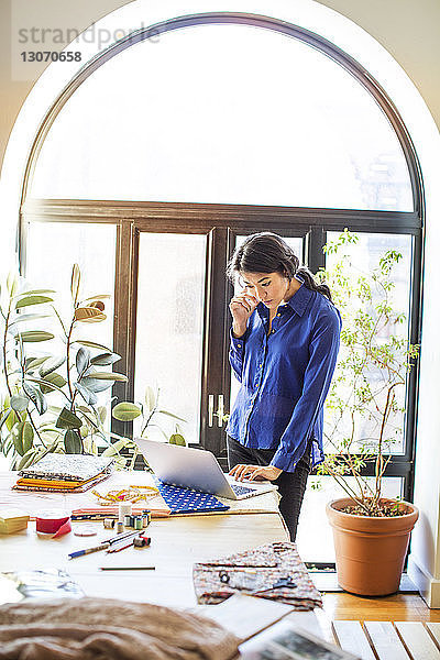 Modedesigner mit Smartphone und Laptop am Schreibtisch im Büro