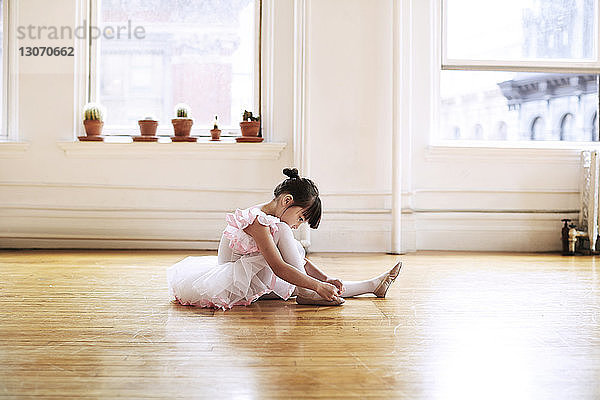 Seitenansicht eines Mädchens in Ballettschuhen  das auf einem Parkettboden im Studio sitzt