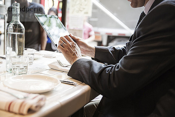 Seitenansicht eines Geschäftsmannes  der einen Tablet-Computer benutzt  während er am Tisch im Restaurant sitzt
