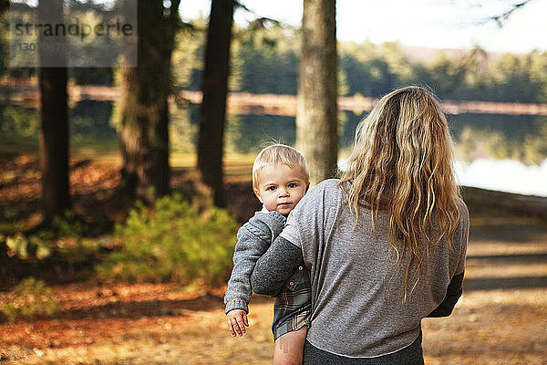 Rückansicht einer Frau  die beim Gehen auf dem Feld ein Baby trägt