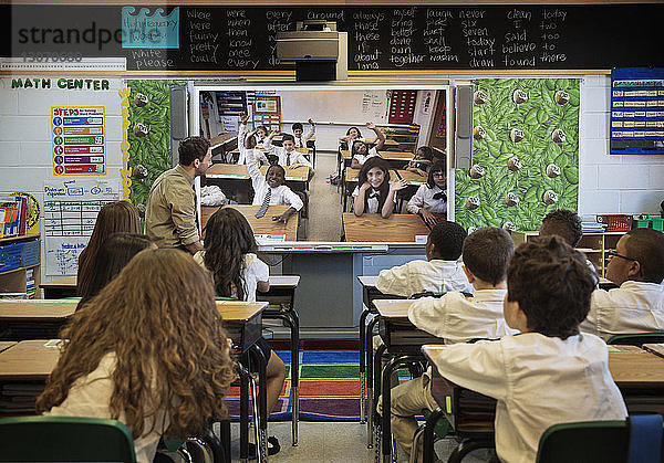 Rückansicht von Schülerinnen und Schülern  die Fotos auf einem Projektionsschirm betrachten  während sie am Schreibtisch im Klassenzimmer sitzen