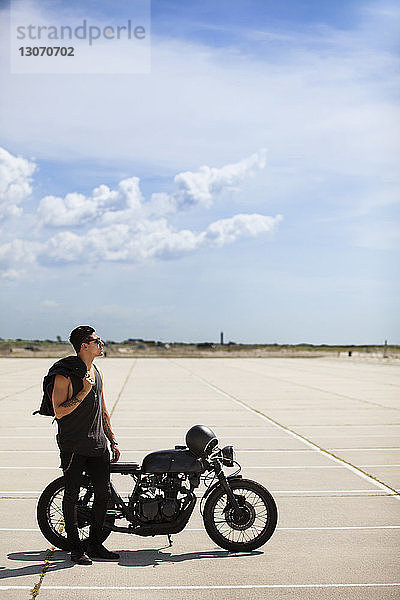 Mann steht mit Motorrad am Feld vor bewölktem Himmel