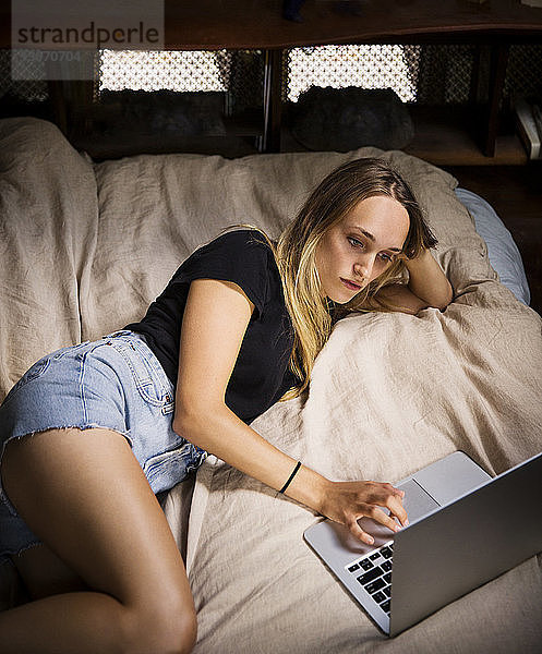 Hochwinkelansicht einer Frau  die einen Laptop-Computer benutzt  während sie auf dem Bett liegt