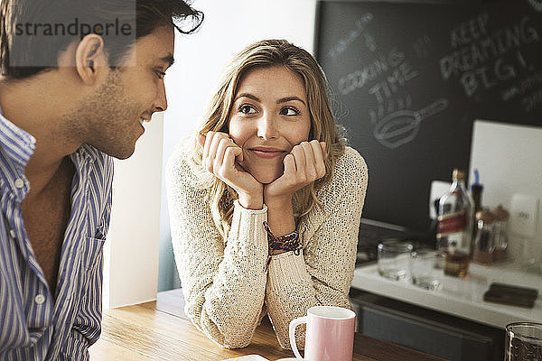 Lächelnde Frau schaut den Mann an  während sie sich zu Hause an den Tisch lehnt