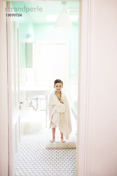 Porträt eines in ein Handtuch gewickelten Jungen im Badezimmer stehend