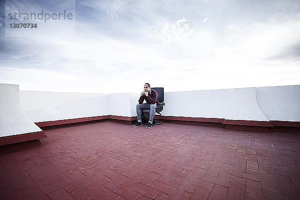 Nachdenklicher Mann sitzt auf Stuhl auf Gebäudeterrasse