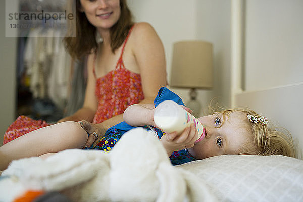Mädchen trinkt Milch  während die Mutter zu Hause am Bett sitzt