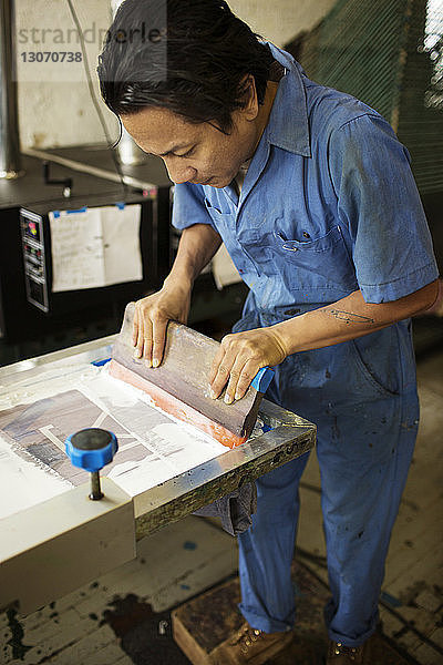 Hochwinkelansicht eines Mannes  der in der Werkstatt Tinte auf einen Rahmen drückt