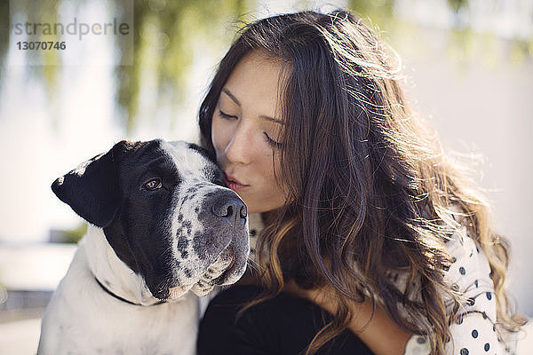 Junge Frau mit langen Haaren küsst Hund an sonnigem Tag