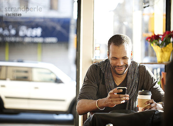 Mann benutzt Mobiltelefon  während er im Cafe sitzt