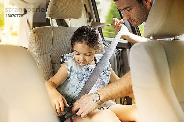 Mann befestigt Sicherheitsgurt für Tochter im Auto