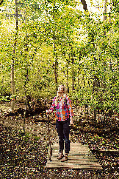 Frau schaut auf  während sie auf einem Steg im Wald steht