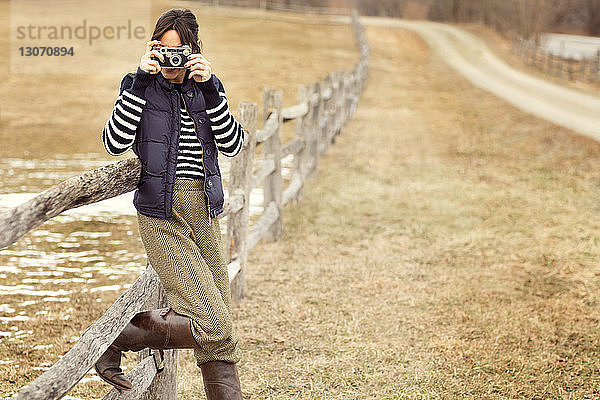 Frau fotografiert im Stehen am Holzgeländer auf dem Feld