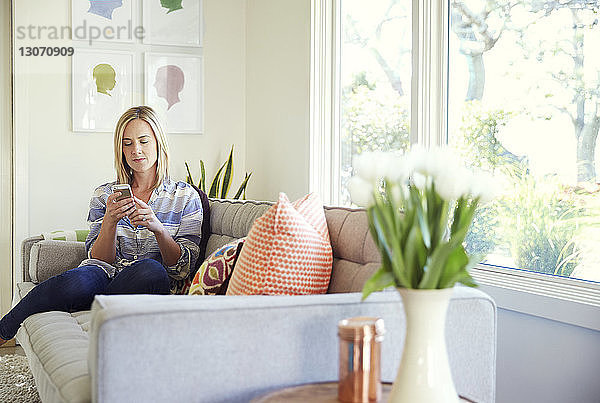 Frau benutzt Mobiltelefon  während sie zu Hause auf dem Sofa sitzt